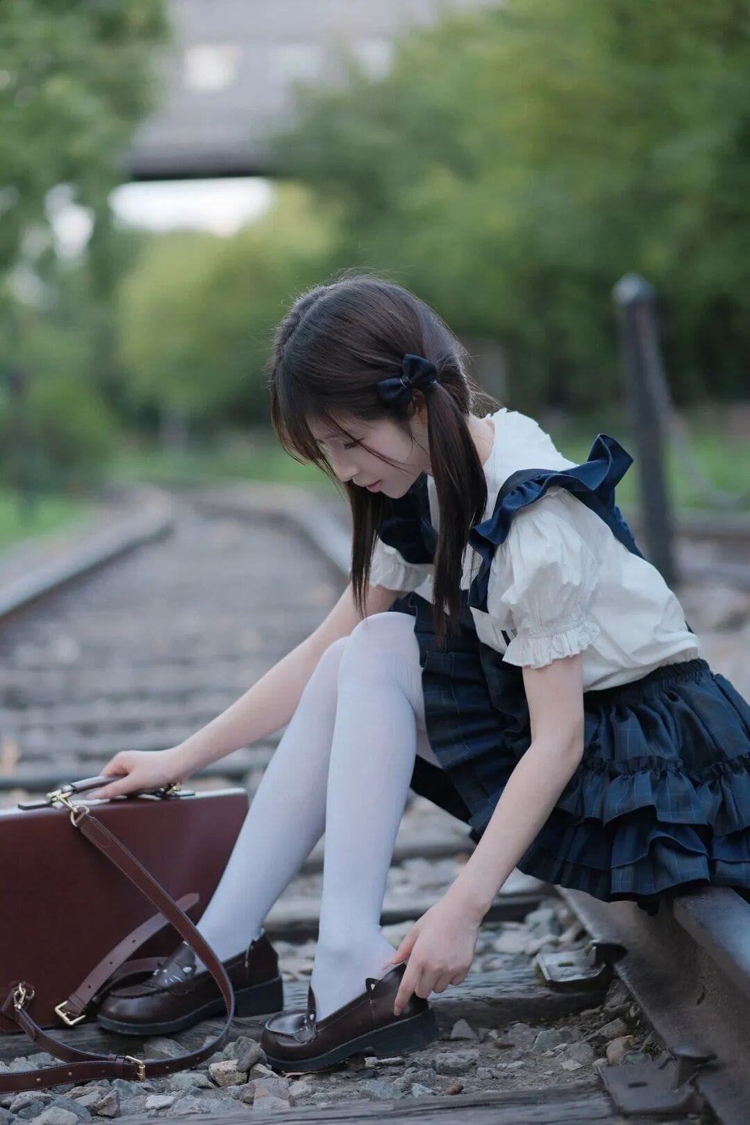 Girl sitting on railway tracks adjusting her shoe beside a brown briefcase