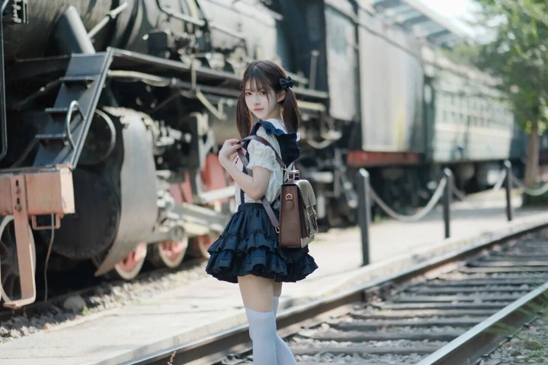 Full view of a girl looking back while standing on railway tracks beside a historic steam locomotive