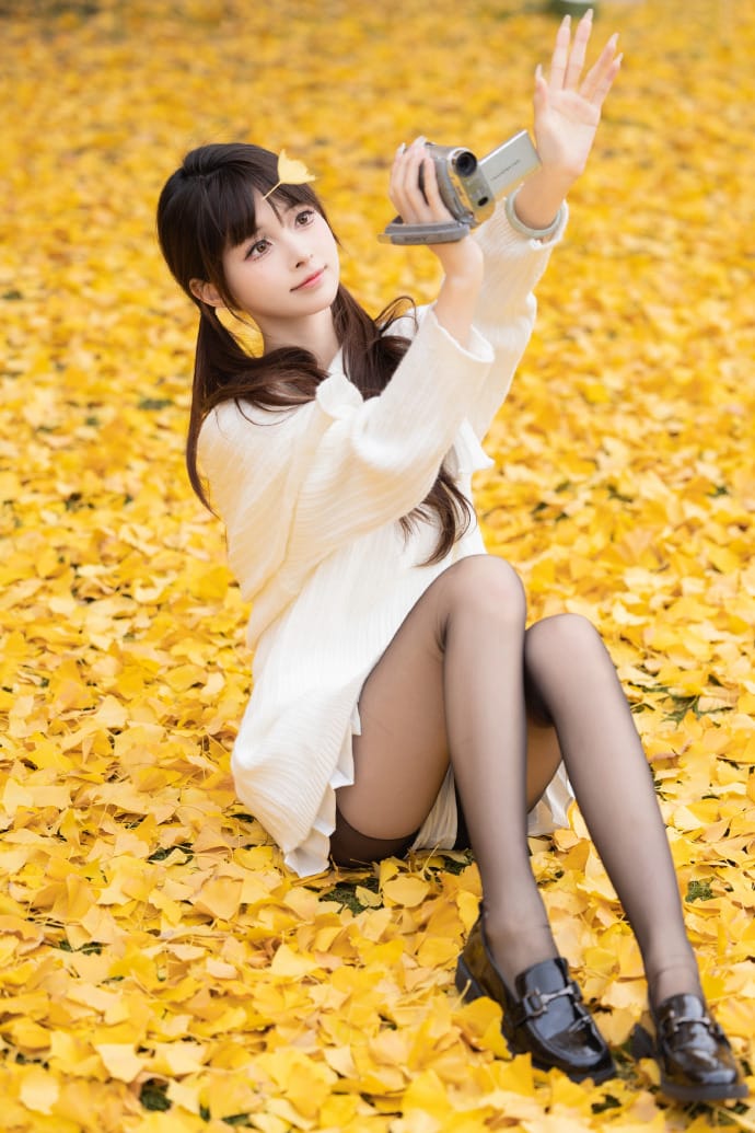 Hetun Nako sitting on a bed of ginkgo leaves holding a vintage camcorder
