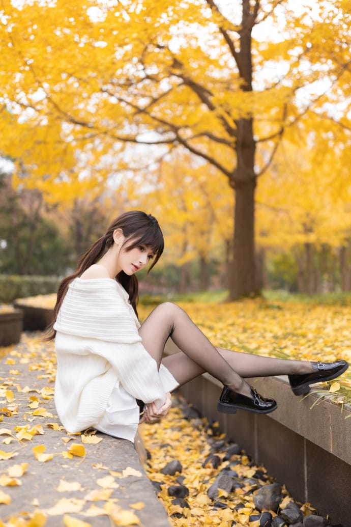 Hetun Nako sitting thoughtfully on a stone ledge framed by golden foliage