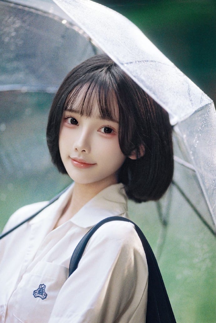 Close-up portrait of Ah Xuan with short dark hair looking gently into the camera under a clear umbrella