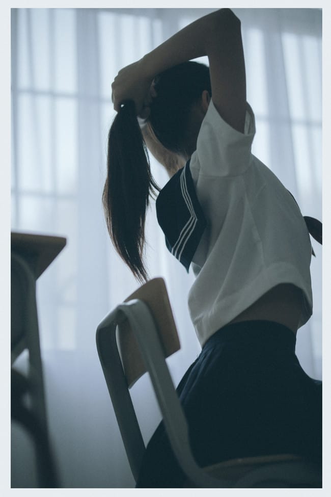 Sukii阿蛊 tying her hair into a ponytail against a bright window