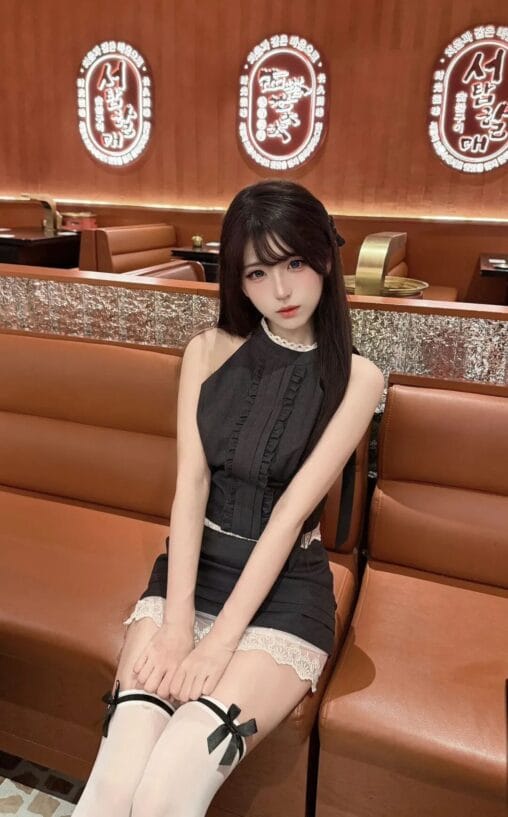 Girl in a chic black lace-trimmed dress sitting on a leather booth