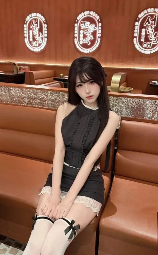 Girl in a chic black lace-trimmed dress sitting on a leather booth