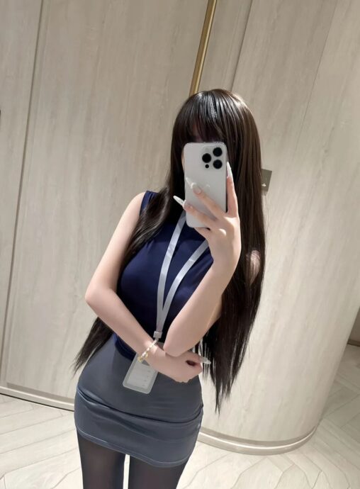Office lady standing in a navy blue sleeveless top and grey fitted skirt holding a phone