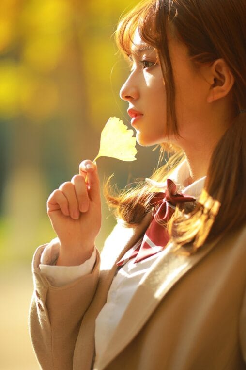 Aesthetic Japanese academy girl holding a golden ginkgo leaf under warm autumn backlight photography by GWJ Wenwen