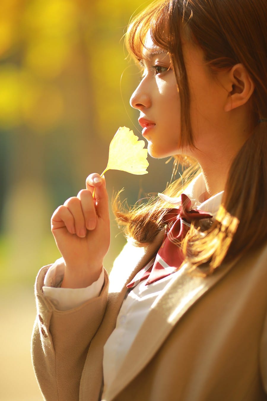 Aesthetic Japanese academy girl holding a golden ginkgo leaf under warm autumn backlight photography by GWJ Wenwen