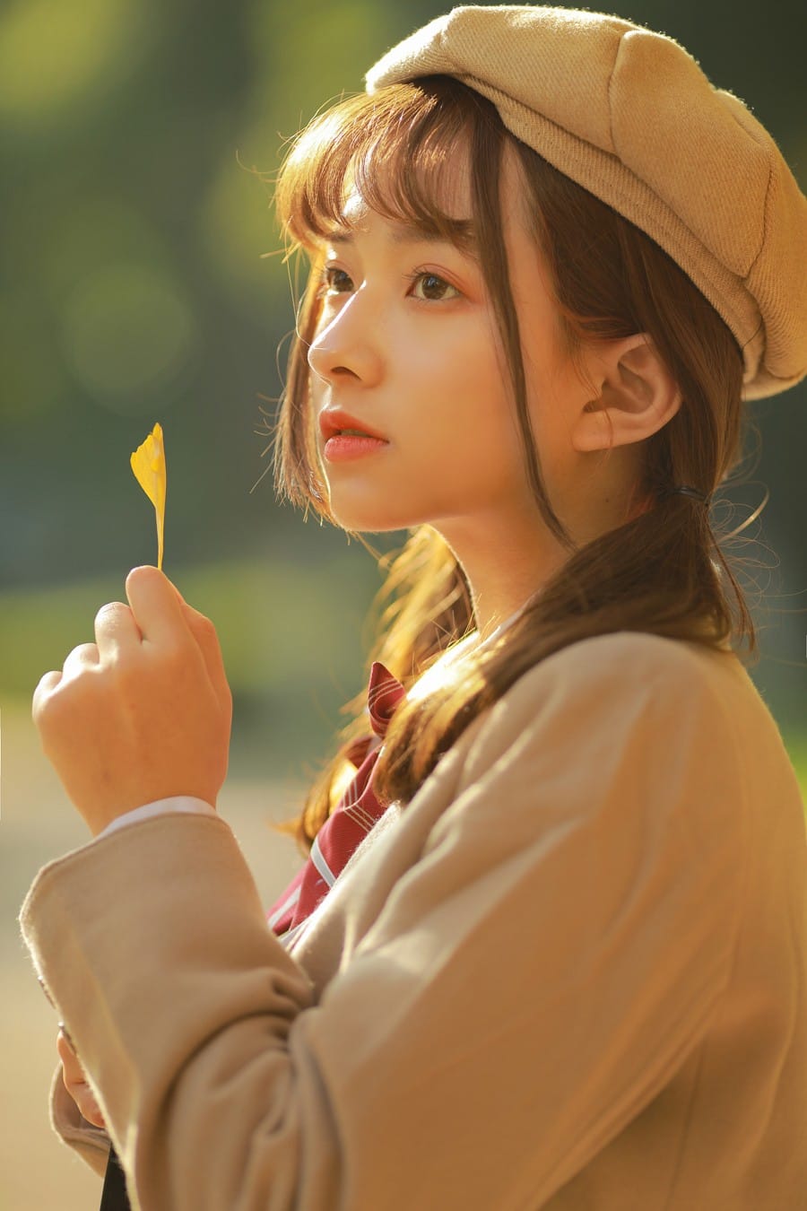 Soft cinematic profile portrait of a girl in beret looking into the distance with ginkgo leaf