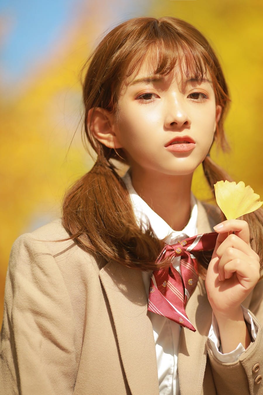 Close-up portrait of a girl with twin tails holding a leaf in autumn sunlight photography by GWJ Wenwen